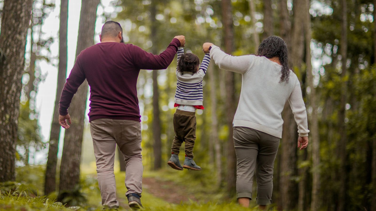 Parents lifting up a young child on a walk in the woods 