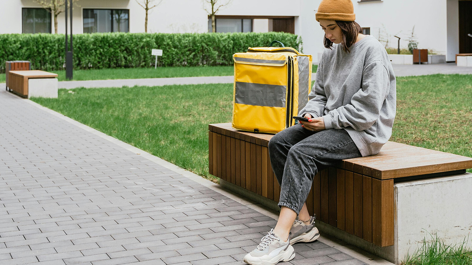 Woman on a bench in front of an apartment building with bag. 